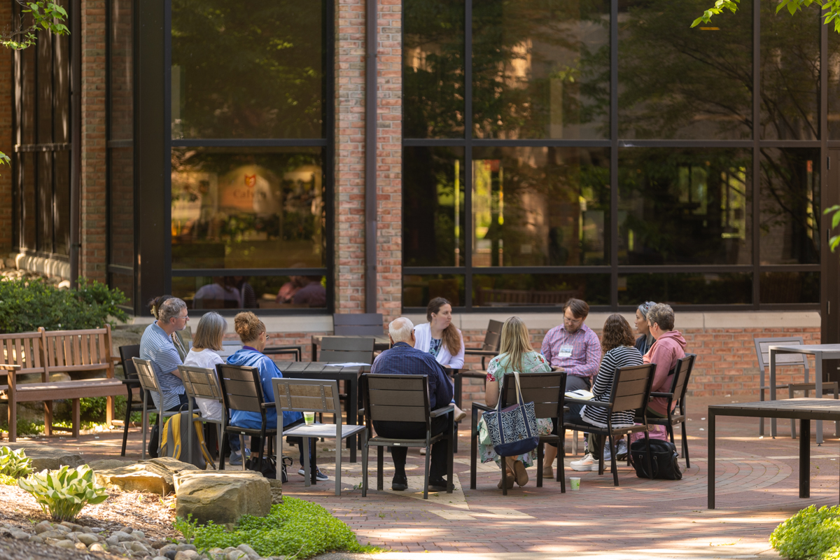A group of people seated in chairs that form a circle outside a brick building.
