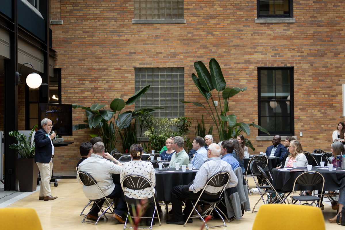 Attendants of the 2024 Calvin University regional gathering seated at round tables, listening to a speaker.
