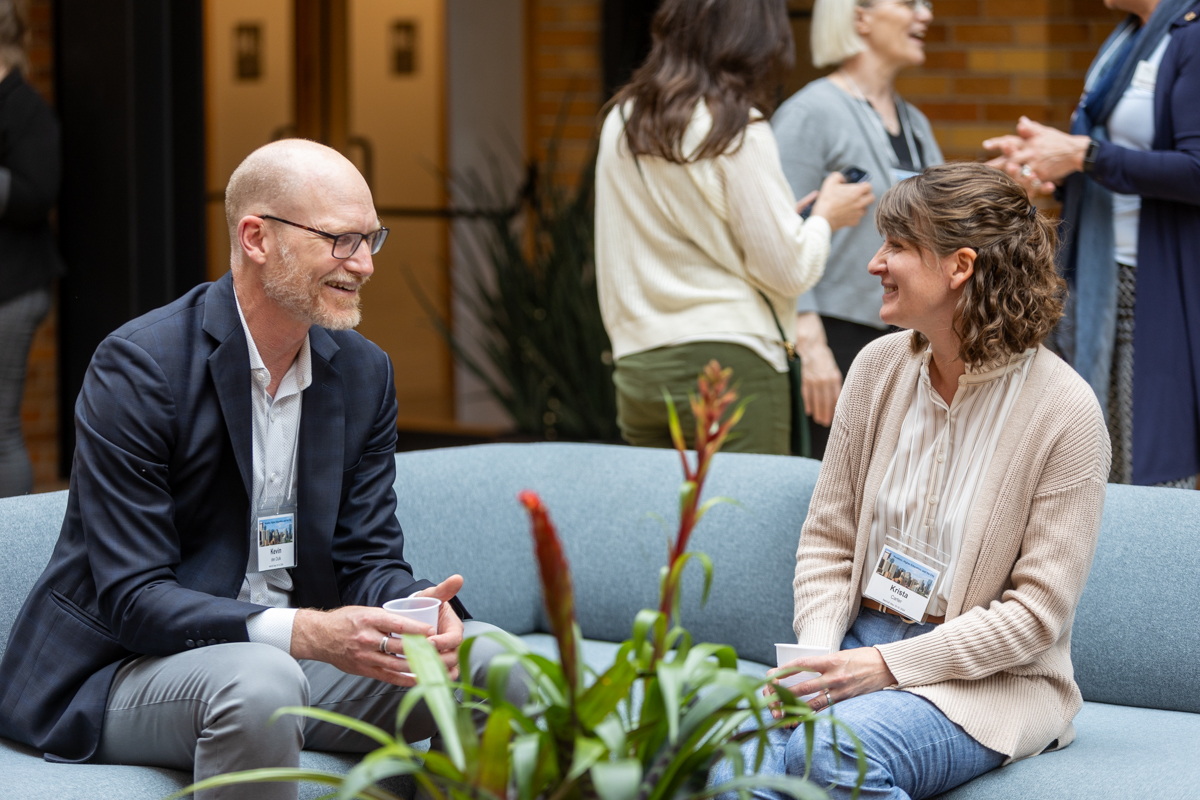Two people seated on a couch, talking with each other.