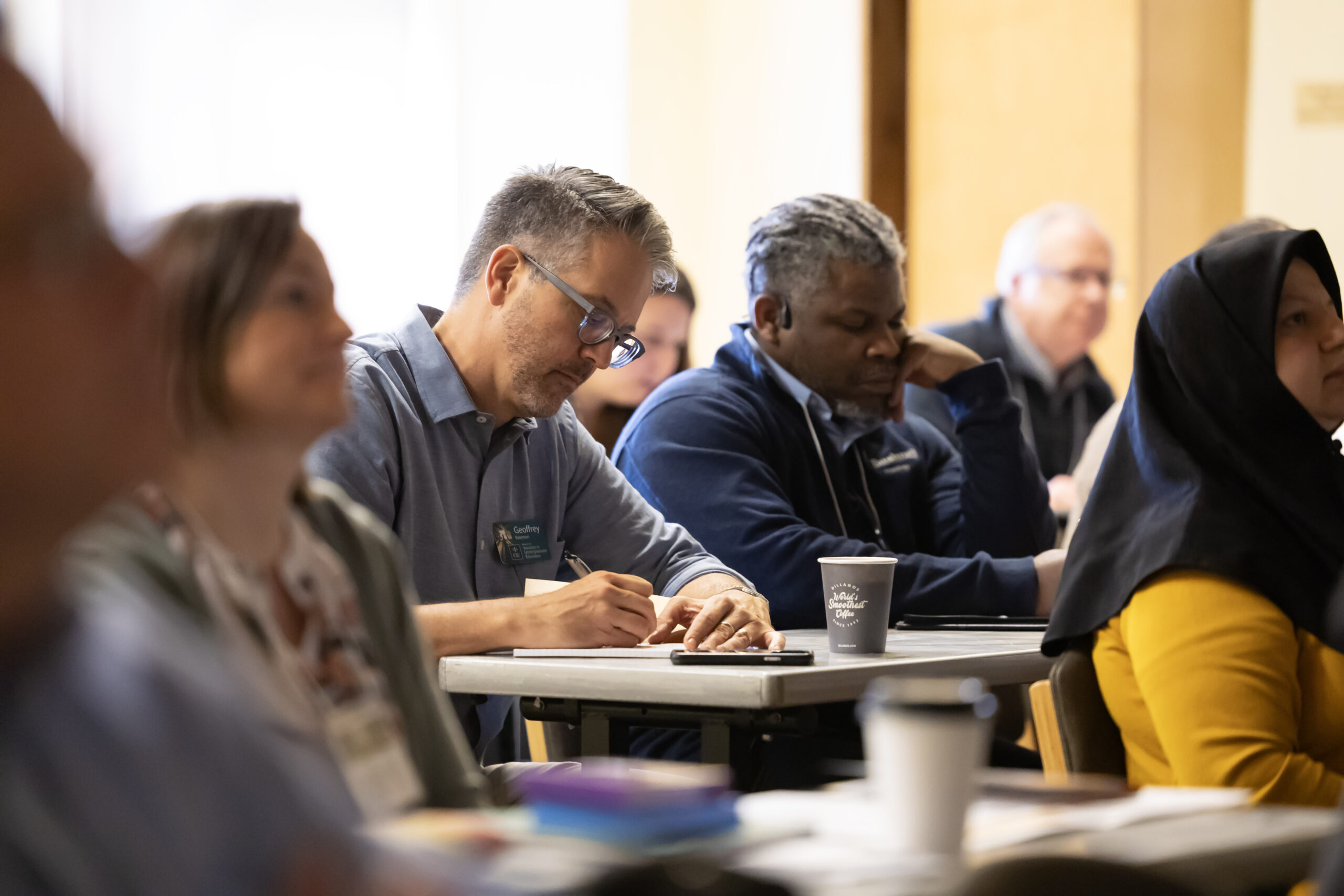 A man taking notes, surrounded by other gathering attendants.